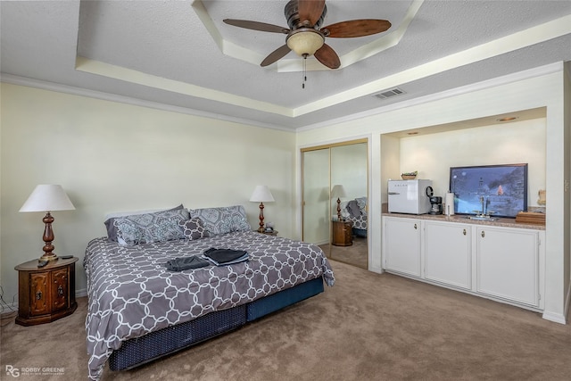 carpeted bedroom with a tray ceiling, ceiling fan, a closet, and a textured ceiling