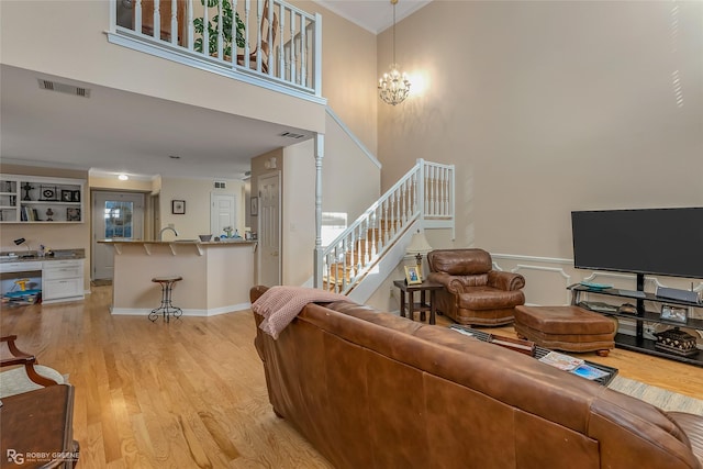 living room with a chandelier, a towering ceiling, light hardwood / wood-style floors, and ornamental molding