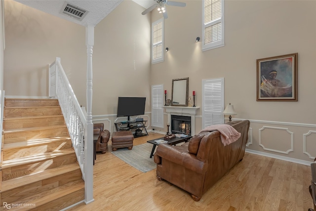 living room featuring ceiling fan, a high ceiling, light hardwood / wood-style floors, and a textured ceiling