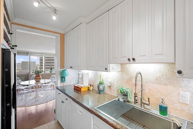 kitchen featuring white dishwasher, sink, dark stone countertops, a textured ceiling, and white cabinetry