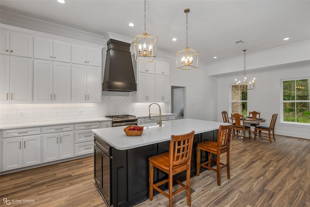 kitchen featuring custom exhaust hood, a kitchen island with sink, white cabinets, sink, and a kitchen bar