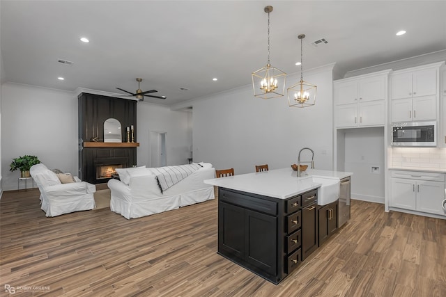 kitchen featuring sink, a fireplace, white cabinets, a center island with sink, and appliances with stainless steel finishes