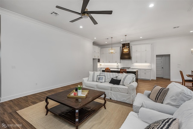 living room featuring ceiling fan, sink, wood-type flooring, and ornamental molding