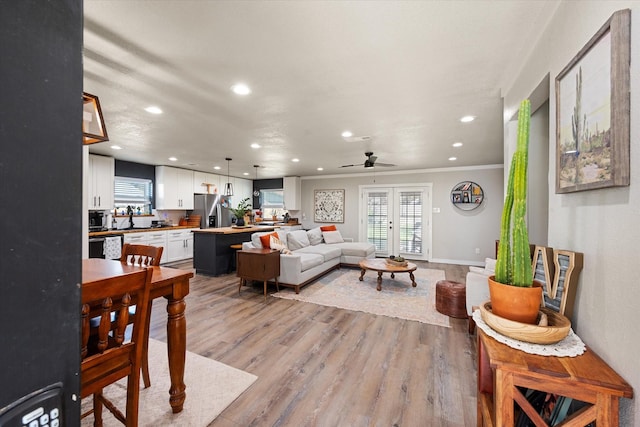 living room with light wood-type flooring, french doors, ceiling fan, and crown molding