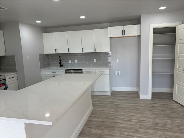 kitchen with light stone countertops, light wood-type flooring, white cabinetry, and dishwasher