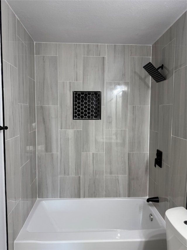 bathroom featuring a textured ceiling, toilet, and tiled shower / bath combo