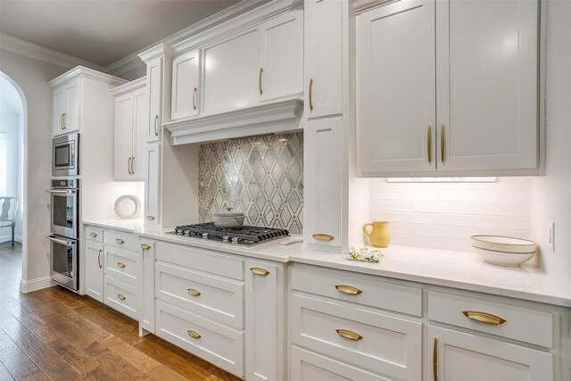 kitchen featuring appliances with stainless steel finishes, backsplash, crown molding, dark hardwood / wood-style floors, and white cabinetry