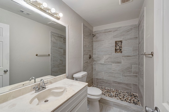 bathroom with tiled shower, vanity, and toilet