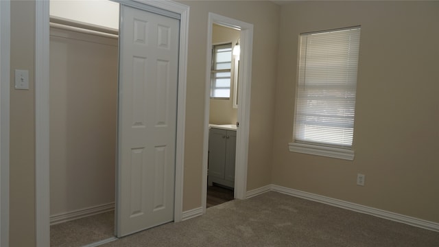 unfurnished bedroom with carpet, connected bathroom, a closet, and multiple windows