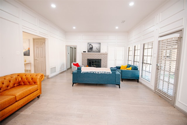 living room with light wood-type flooring, a brick fireplace, and ornamental molding