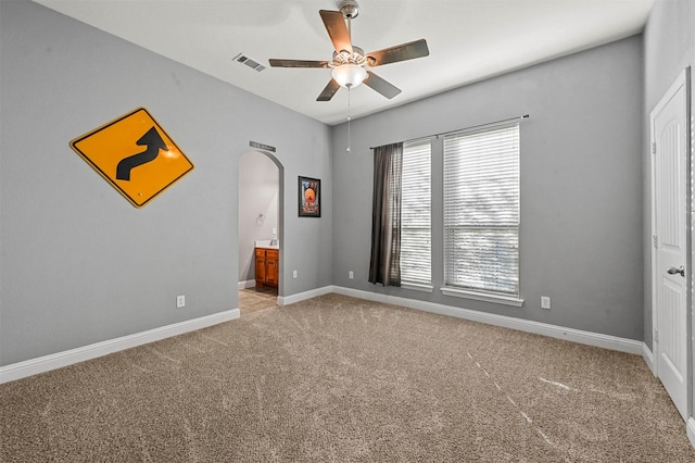 spare room featuring light carpet, baseboards, visible vents, arched walkways, and a ceiling fan