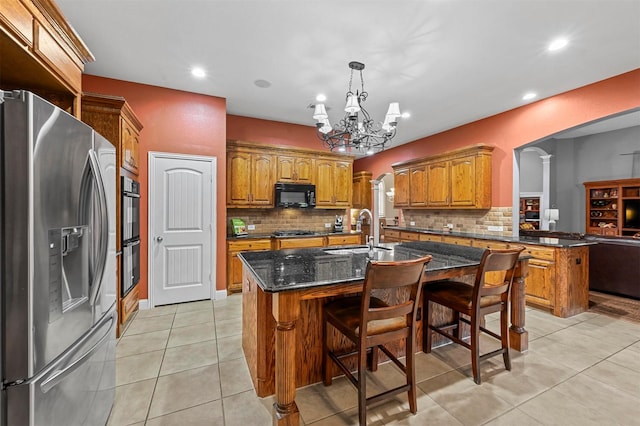 kitchen with a center island with sink, brown cabinets, black appliances, a kitchen bar, and a sink