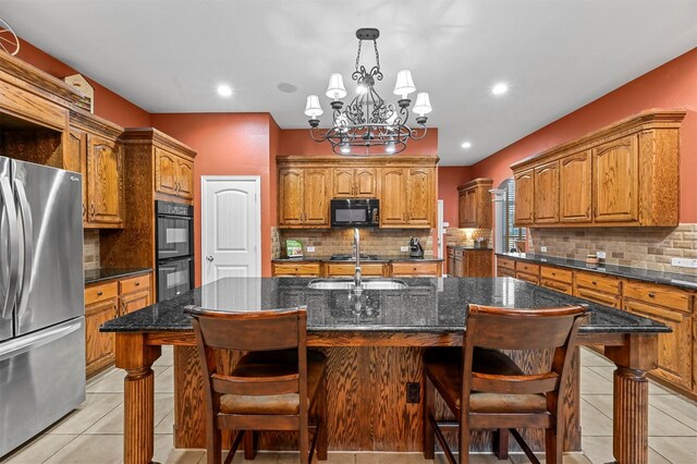 kitchen featuring brown cabinets, a kitchen island with sink, black appliances, a kitchen bar, and light tile patterned flooring