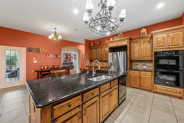 kitchen with pendant lighting, a sink, black appliances, a center island with sink, and an inviting chandelier