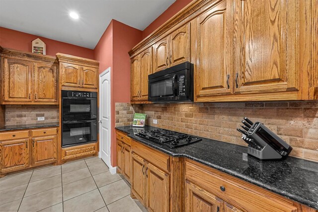 kitchen with light tile patterned flooring, decorative backsplash, black appliances, brown cabinetry, and dark stone countertops