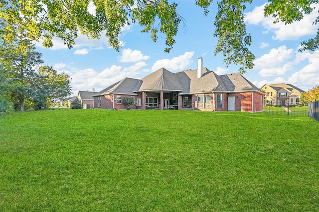 rear view of property with brick siding, a lawn, a chimney, and fence