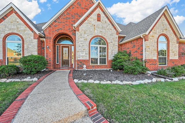 view of front of property featuring roof with shingles, brick siding, and a front lawn