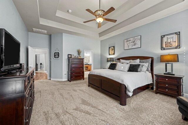 bedroom featuring a raised ceiling, visible vents, light colored carpet, ensuite bath, and baseboards