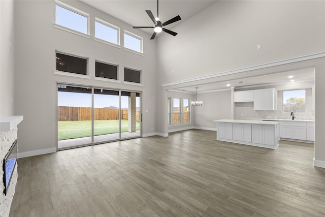 unfurnished living room featuring sink, ceiling fan with notable chandelier, wood-type flooring, and a high ceiling