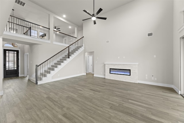 unfurnished living room with ceiling fan, a towering ceiling, and light hardwood / wood-style flooring