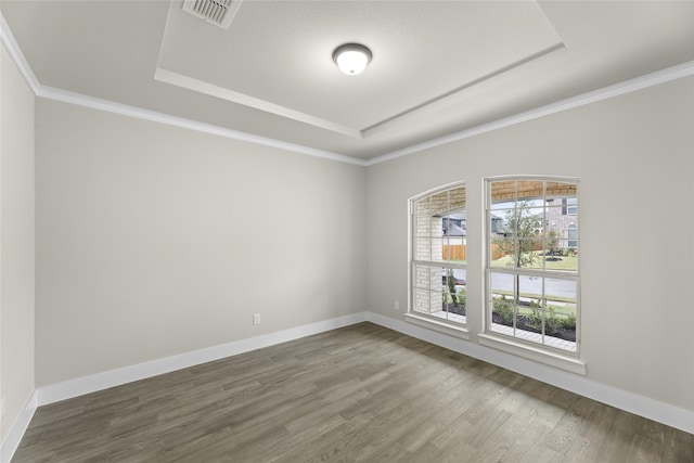 empty room with a raised ceiling, dark wood-type flooring, and ornamental molding