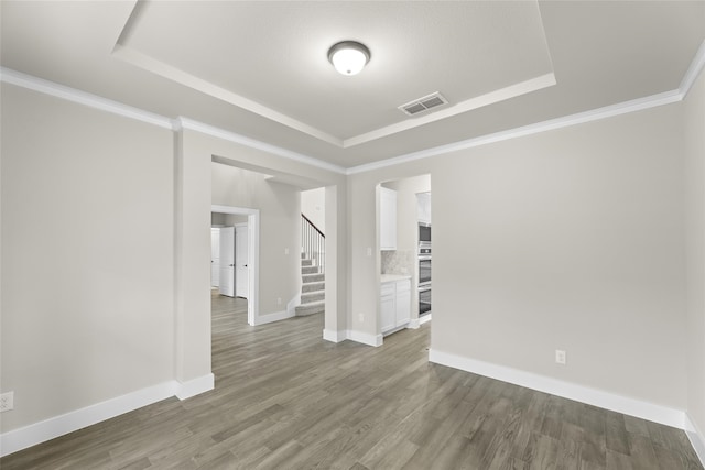 empty room featuring a tray ceiling, dark wood-type flooring, and ornamental molding