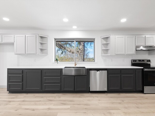 kitchen with backsplash, sink, light wood-type flooring, appliances with stainless steel finishes, and white cabinetry