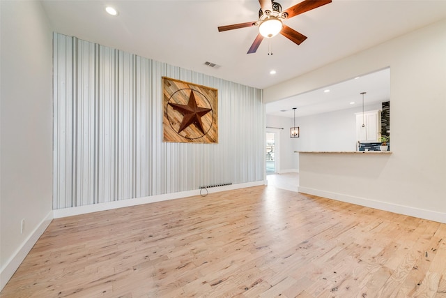 empty room featuring ceiling fan with notable chandelier and light hardwood / wood-style floors