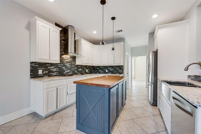 kitchen with appliances with stainless steel finishes, white cabinetry, butcher block counters, and wall chimney range hood