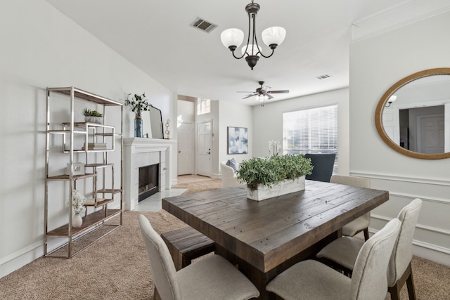 dining room featuring light carpet, ceiling fan with notable chandelier, and a tile fireplace