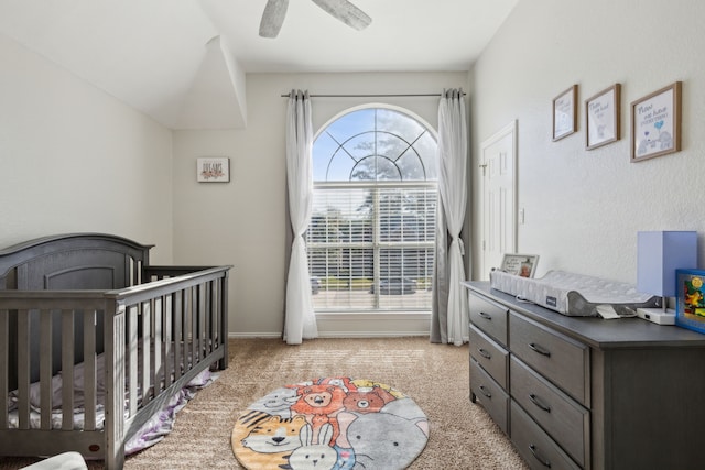 bedroom featuring light colored carpet, a nursery area, and ceiling fan