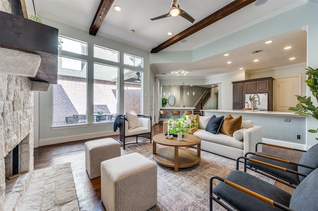 living room with hardwood / wood-style flooring, ceiling fan, ornamental molding, a fireplace, and beamed ceiling