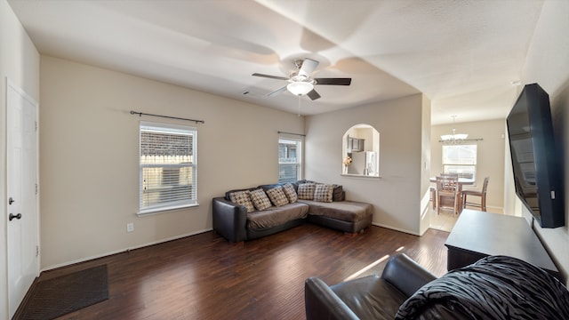 living room with a wealth of natural light, dark wood-type flooring, and ceiling fan with notable chandelier