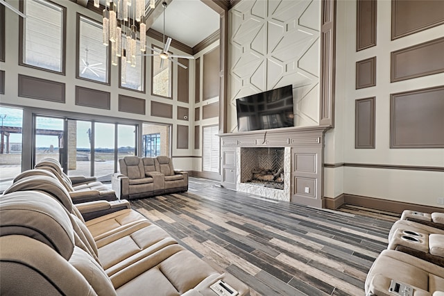 living room with ceiling fan with notable chandelier, ornamental molding, a high ceiling, and hardwood / wood-style flooring