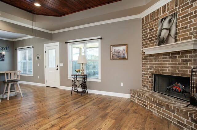 foyer entrance featuring hardwood / wood-style flooring, ornamental molding, wooden ceiling, and a brick fireplace