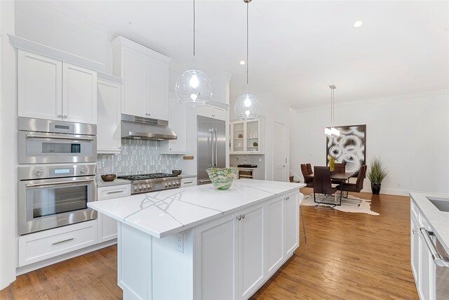 kitchen featuring decorative backsplash, appliances with stainless steel finishes, a center island, under cabinet range hood, and white cabinetry