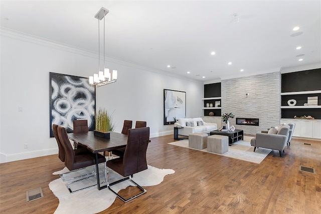 dining area featuring light wood-type flooring, a large fireplace, ornamental molding, and built in features