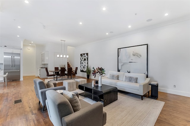 living room featuring light hardwood / wood-style flooring, ornamental molding, and a notable chandelier