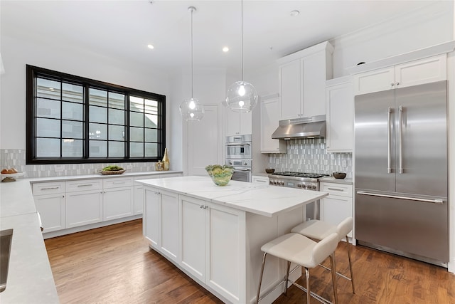 kitchen featuring tasteful backsplash, appliances with stainless steel finishes, a center island, under cabinet range hood, and white cabinetry