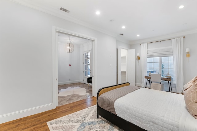 bedroom with ornamental molding, wood finished floors, visible vents, and baseboards