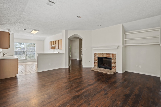 unfurnished living room featuring sink, dark hardwood / wood-style flooring, a textured ceiling, and a brick fireplace