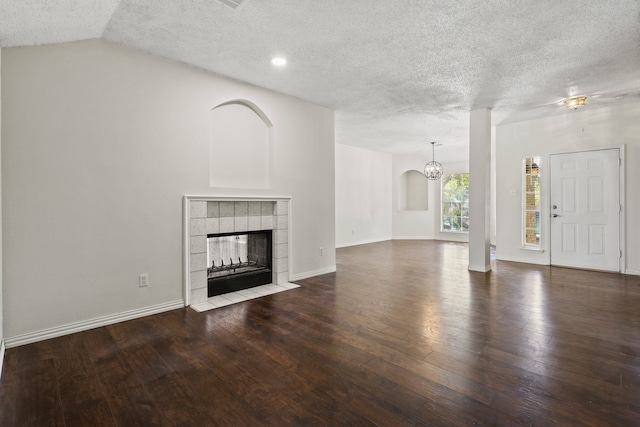 unfurnished living room featuring a textured ceiling, a tiled fireplace, dark wood-type flooring, and lofted ceiling