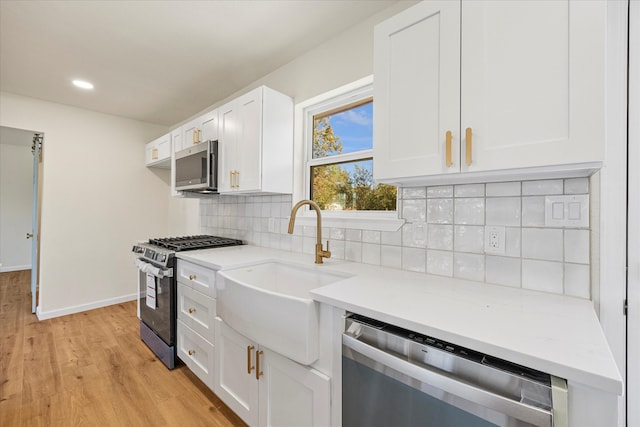 kitchen featuring white cabinetry, sink, stainless steel appliances, tasteful backsplash, and light wood-type flooring