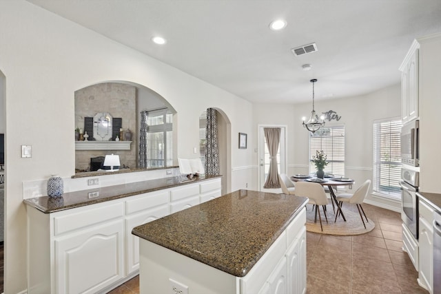 kitchen featuring appliances with stainless steel finishes, a kitchen island, a notable chandelier, dark stone countertops, and white cabinetry