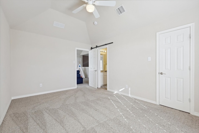 unfurnished bedroom with ceiling fan, a barn door, light colored carpet, and vaulted ceiling