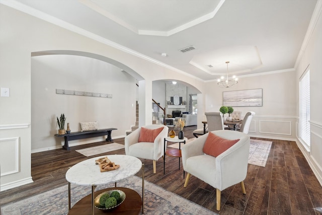 living room featuring a tray ceiling, a notable chandelier, dark hardwood / wood-style floors, and ornamental molding