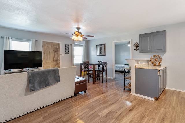 living room with a textured ceiling, light hardwood / wood-style floors, ceiling fan, and a healthy amount of sunlight