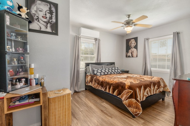 bedroom featuring an AC wall unit, multiple windows, ceiling fan, and hardwood / wood-style floors