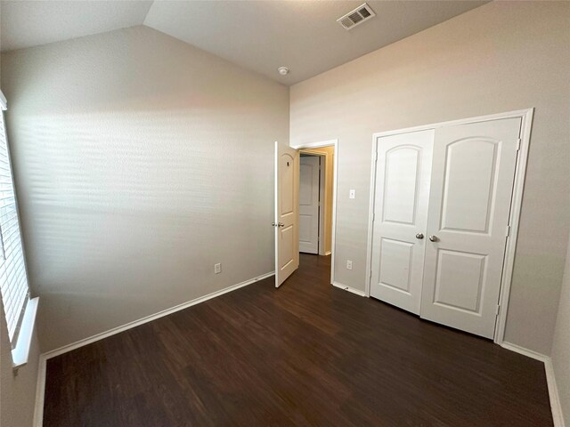 unfurnished bedroom with dark hardwood / wood-style floors, lofted ceiling, and a closet