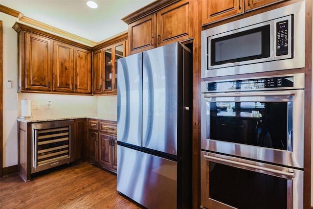 kitchen with beverage cooler, dark wood-type flooring, appliances with stainless steel finishes, light stone countertops, and glass insert cabinets